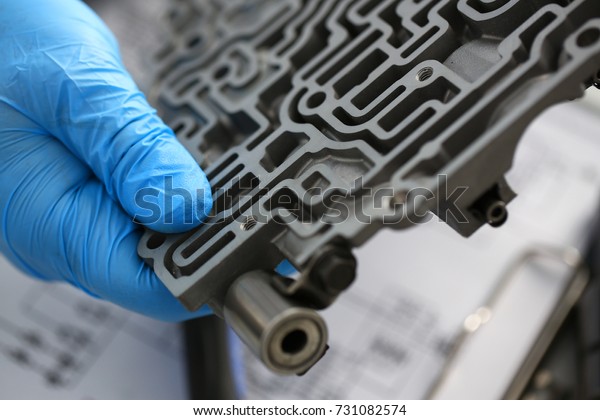The auto repair service repairman in automatic\
gearboxes holds in his hand in blue protective gloves the\
hydroblock detail dehydrates the diagnostics and estimates the\
detail test transmission\
closeup