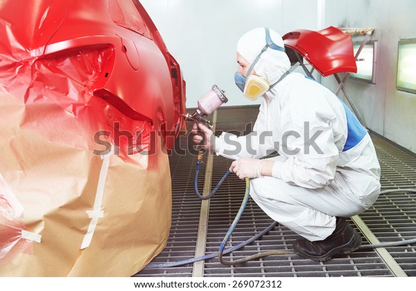 auto repair worker painting a red car in a paint\
chamber during repair work