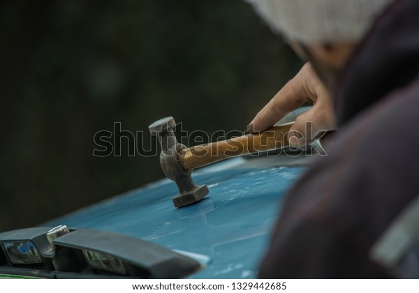 Auto repair worker straightening dents in metal\
car sheet or body using a hammer. Special body panel hammer being\
used by a home mechanic\
outdoors
