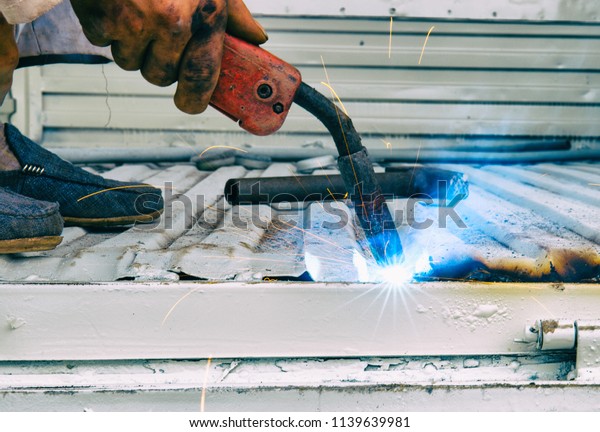 An auto repair worker is using\
electric welding to connect the car\'s cargo box\
outdoors