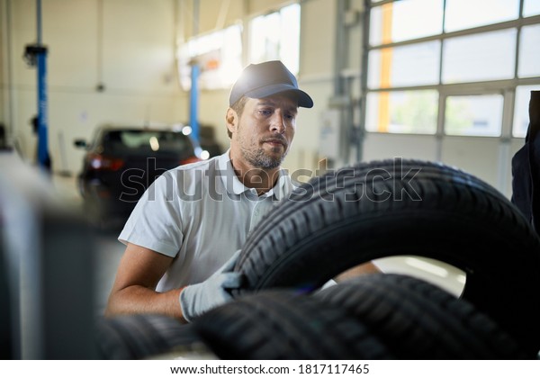 Auto repairman stacking car tires on a rack while\
working in a workshop. 