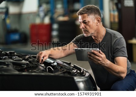 Auto repairman using touchpad while examining car engine in a workshop. 