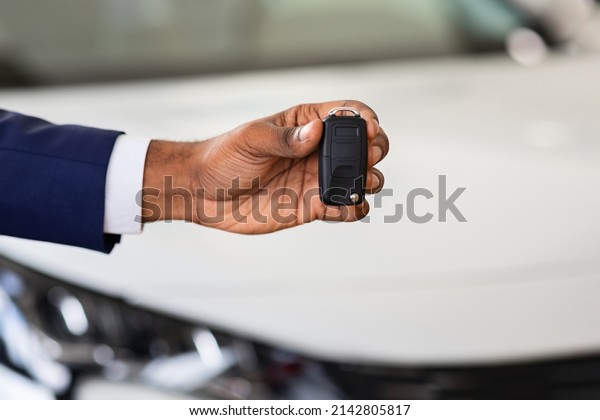 Auto Sale Concept. Closeup Of Car Keys In African\
American Man Hand, Unrecognizable Black Male Dealership Center\
Manager In Suit Holding Automobile Key Over Luxury Vehicle On\
Background, Cropped