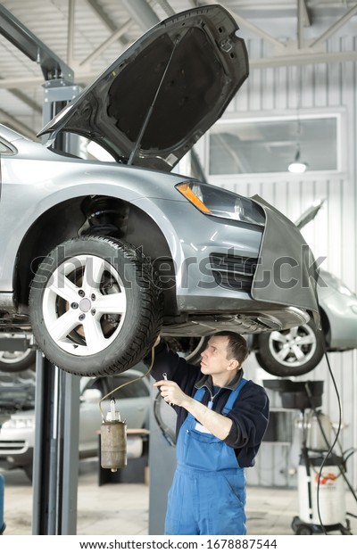 Auto service.\
Car mechanic worker replacing brake liquid of lifted automobile at\
repair garage shop station