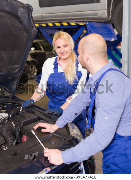 Auto service center crew\
with attractive young blonde repairing a broken car at garage.\
Focus on girl