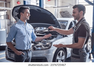 At the auto service. Handsome young auto mechanic in uniform is returning car key to a client, both are smiling - Powered by Shutterstock