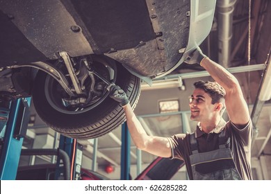 At the auto service. Handsome young auto mechanic in uniform is smiling while repairing car - Powered by Shutterstock