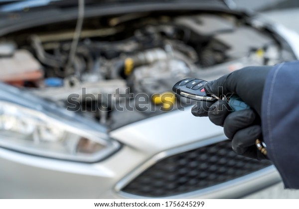 Auto service mechanic hold keys in hand\
 with car on the background, open hood.\
Repair