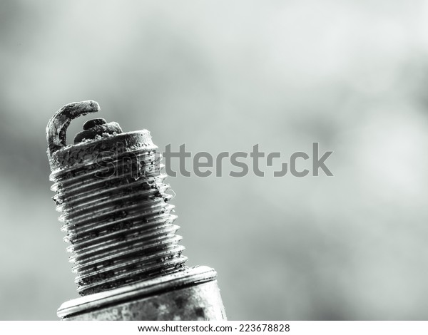 Auto service. Old car spark plug\
as spare part of auto transportation on blurry gray\
background.