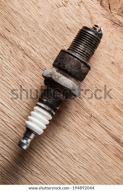 Auto service. Old rusty spark plug\
as spare part of car transportation on wooden\
background.