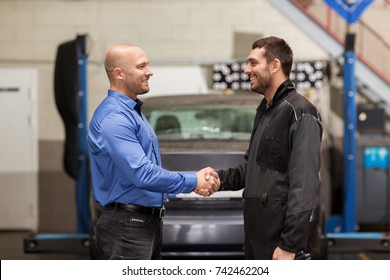 Auto Service, Repair, Deal And People Concept - Mechanic And Customer Or Car Owner Shaking Hands At Workshop