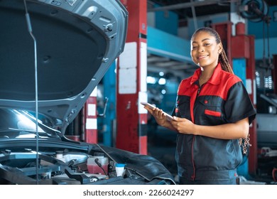 Auto service, repair, maintenance concept. Mechanic checks the car at the service station.African american woman  looking at camera engineer use tablet check car battery .