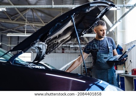 Auto service, repair, maintenance concept. mechanic checks the car, making diagnostics with laptop at the service station. Service maintenance of industrial to engine repair.