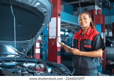 Auto service, repair, maintenance concept. Mechanic checks the car at the service station.African american woman  looking at camera engineer use tablet check car battery .