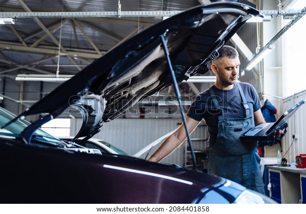Auto service,\
repair, maintenance concept. mechanic checks the car, making\
diagnostics with laptop at the service station. Service maintenance\
of industrial to engine\
repair.