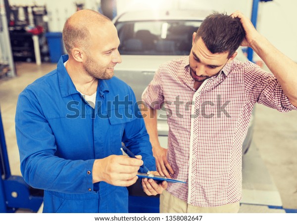 auto\
service, repair, maintenance and people concept - mechanic with\
clipboard talking to man or owner at car\
shop