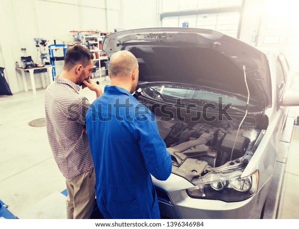 auto service, repair,\
maintenance and people concept - mechanic and man or car owner at\
workshop