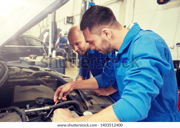 auto service, repair,\
maintenance and people concept - mechanic men with wrench repairing\
car at workshop