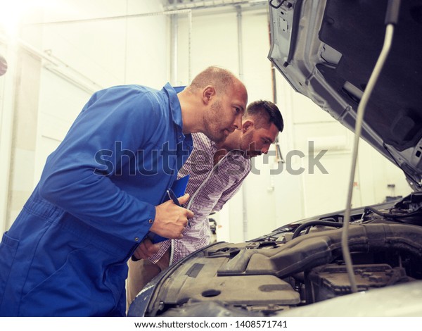 auto service, repair, maintenance and people concept\
- mechanic with clipboard and man or owner looking at broken car at\
shop