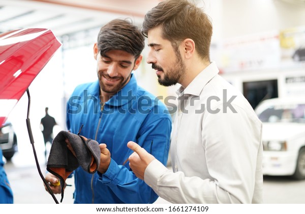 auto service, repair, maintenance and\
people concept.Mechanic showing customer the problem at broken car\
engine with car at the repair garage repair\
shop