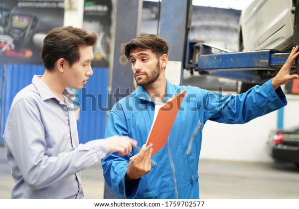 auto service, repair, maintenance and\
people concept.Mechanic showing customer the problem at broken car\
engine with car at the repair garage repair\
shop