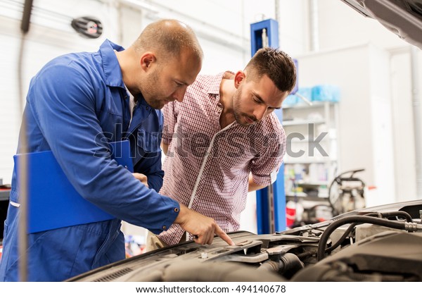 auto service, repair, maintenance and people concept\
- mechanic with clipboard and man or owner looking at broken car\
engine at shop