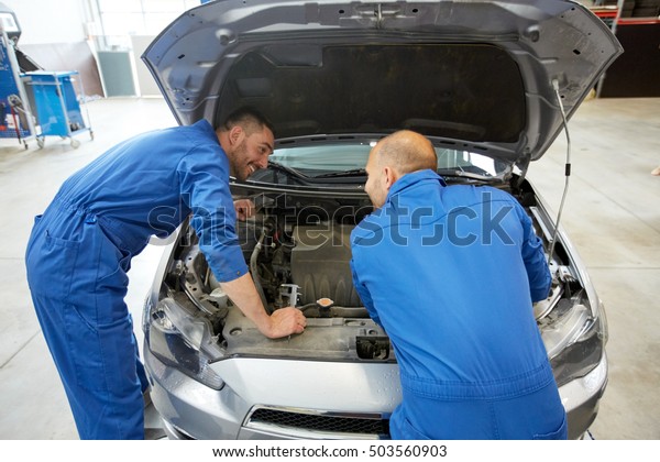 auto service, repair,\
maintenance and people concept - mechanic men with wrench repairing\
car at workshop