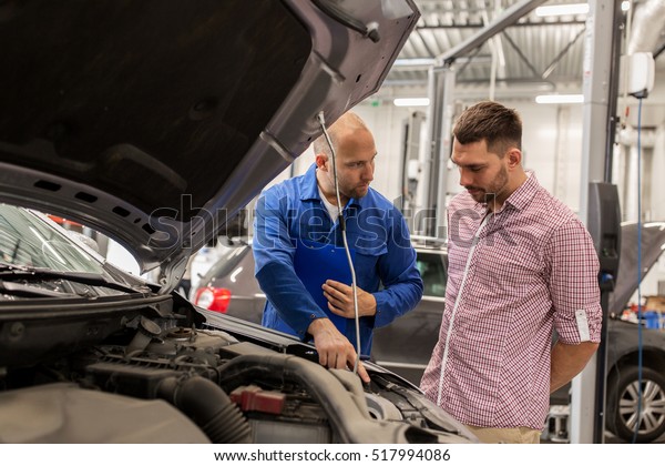 auto\
service, repair, maintenance and people concept - mechanic with\
clipboard talking to man or owner at car\
shop