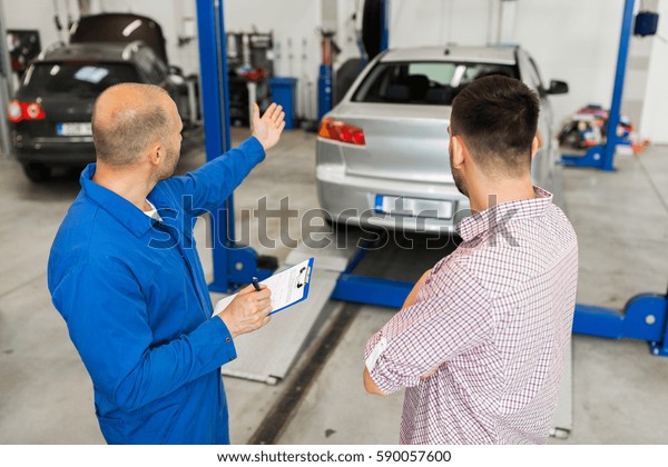 auto
service, repair, maintenance and people concept - mechanic with
clipboard talking to man or owner at car
shop