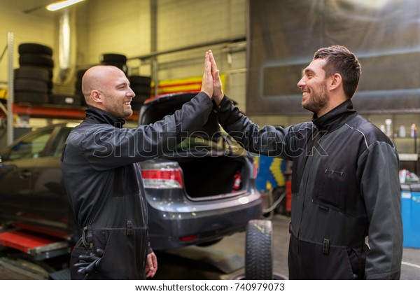 auto service,\
repair, maintenance and people concept - mechanics or tire changers\
making high five at car\
shop