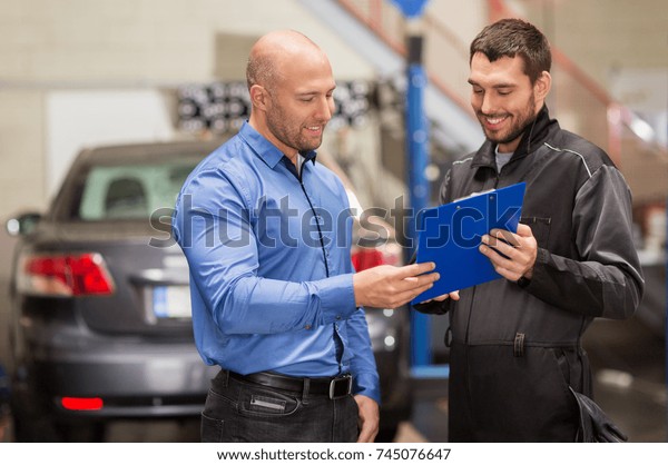 auto\
service, repair, maintenance and people concept - mechanic with\
clipboard and customer or car owner at\
workshop