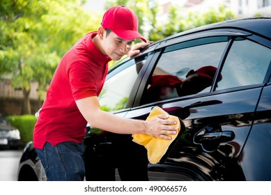 Auto service staff in red uniform cleaning car with microfiber cloth - car detailing and valeting concepts