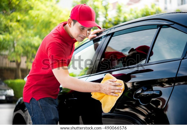 Auto service staff in\
red uniform cleaning car with microfiber cloth - car detailing and\
valeting concepts