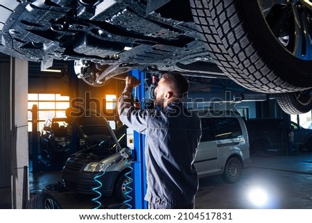 Auto service station background. Mechanic repairs car chassis using a car lift.