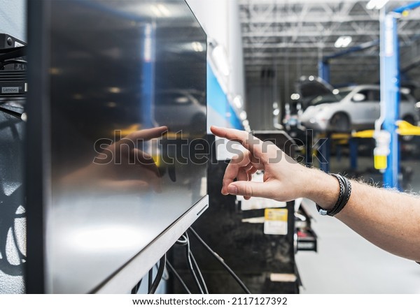 Auto Service\
Technician Looking For Car Parts on His Computer Inside Vehicles\
Service Area. Automotive\
Computer.