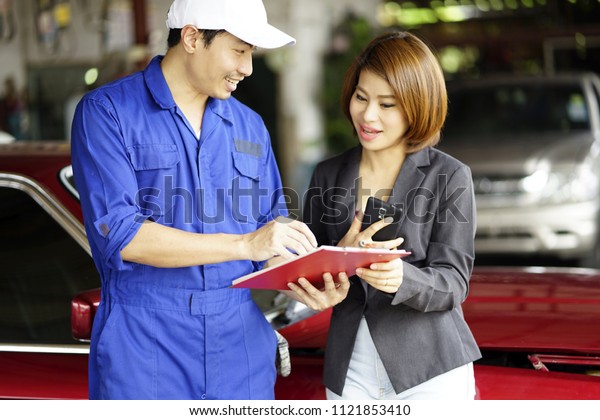 Auto service, Woman customer talking to the car\
mechanic for  repair broken car.  Maintenance and people concept -\
mechanic with clipboard and customer or car owner at workshop.\
Smile customer talking