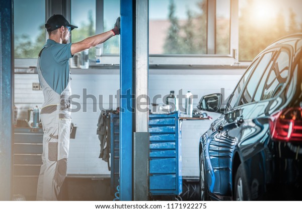 Auto Service Worker in Front\
of Heavy Duty Car Lift. Preparing For the Work. Automotive\
Industry.