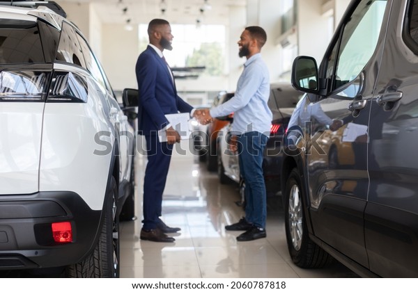 Auto Showroom Manager Shaking Hands With Male\
Customer After Successful Deal, Young African American Man Buying\
Car In Modern Dealership Center, Handshaking With Salesperson,\
Selective Focus