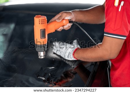 Auto specialist worker hand blowing hot air dryer or hairdryer removing old car window film tint and installing the new one. Car front windscreen film removal and tinting installation