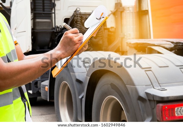 Auto technician holding clipboard inspecting safety\
checklist a truck 