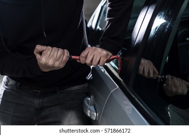 Auto Thief In Black Balaclava Trying To Break Into Car With Crowbar. Car Thief, Car Theft