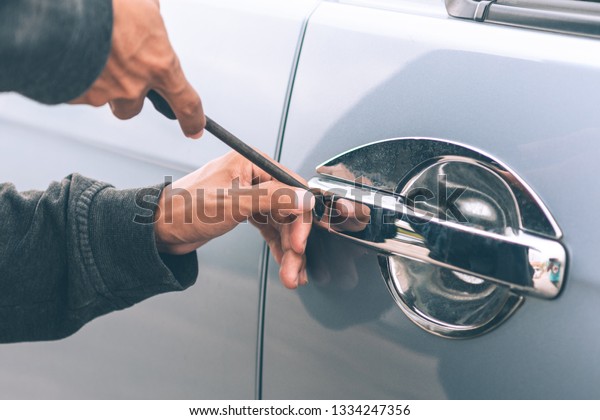 Auto thief in black balaclava trying\
to break into car with screwdriver. Car thief, car\
theft