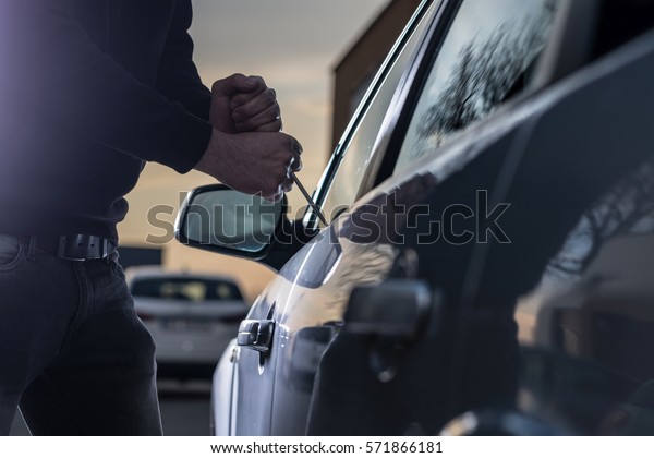 Auto thief in black balaclava trying
to break into car with screwdriver. Car thief, car
theft
