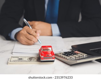 Auto title loan or Car loan. A Businessman signs a contract loan agreement while sitting at the table. Mini a red car model, a calculator, and a laptop on a table. Car finance and insurance concept