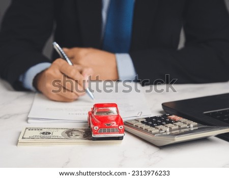 Auto title loan or Car loan. A Businessman signs a contract loan agreement while sitting at the table. Mini a red car model, a calculator, and a laptop on a table. Car finance and insurance concept
