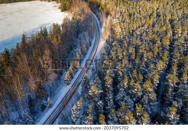 Auto track in winter forest. Northern nature with\
road. Winter track from bird\'s eye view. Winter taiga with empty\
highway. Snowy taiga. Coniferous trees next to automobile highway.\
Auto travel route