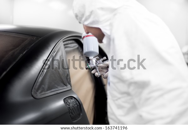 auto worker spraying black paint on a car in an\
auto garage
