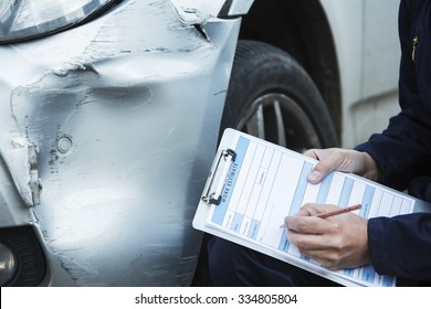 Auto Workshop Mechanic Inspecting Damage To Car And Filling In Repair Estimate