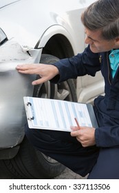 Auto Workshop Mechanic Inspecting Damage To Car And Filling In Repair Estimate