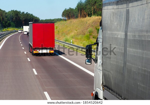 Autobahn in Europe. Cars and trucks, traffic on\
the highway. Truck on foreground, back view, asphalt road in rural\
pine forest landscape